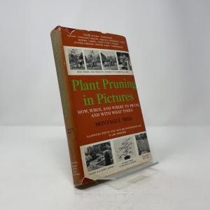 May include: A vintage book titled "Plant Pruning in Pictures" by Montague Free. The cover is orange with green text and features images of plants and gardens. The book is propped up on a clear stand.