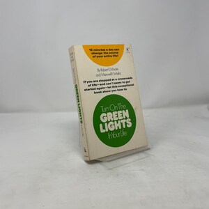 Peut inclure: Un livre de poche vintage intitulé "Turn On The Green Lights In Your Life". La couverture présente un cercle vert avec du texte blanc et le titre du livre. Du texte supplémentaire comprend les noms des auteurs et une citation.