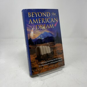 Op de afbeelding: Een hardcover boek getiteld "Beyond the American Dream" met een blauwe omslag. De omslag toont een bergketen, een huifkar en een lancerende raket. De ondertitel van het boek is "Lifelong Learning and the Search for Meaning in a Postmodern World."