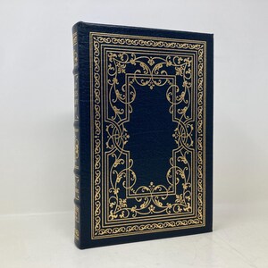 May include: A dark blue hardcover book with a gold-colored decorative border. The border features a floral design.