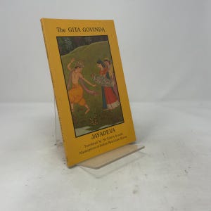 Peut inclure: Un livre de poche jaune intitulé The Gita Govinda de Jayadeva, traduit par Sir Edwin Arnold. La couverture présente une illustration rectangulaire centrale de trois personnages dans un paysage, avec du texte noir imprimé au-dessus et en dessous.