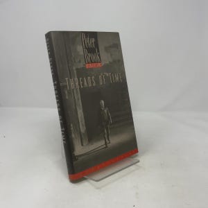 May include: A hardback book titled Threads of Time: Recollections by Peter Brook. The cover features a black and white photograph of a person walking through a doorway, with red accents at the top and bottom edges of the spine and front cover.