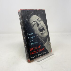 May include: Vintage hardcover book titled "Lady Sings the Blues" by Billie Holiday. The cover features a black and white image of Billie Holiday singing. The book's spine and edges show signs of wear, with the title and author's name clearly visible.