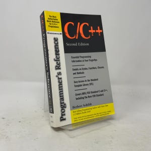Pode incluir: Um livro de bolso intitulado C/C++ Programmer's Reference Second Edition de Herbert Schildt. A capa é preta, cinza e amarela com texto laranja. Contém detalhes sobre sintaxe, funções, classes, métodos e a Standard Template Library.