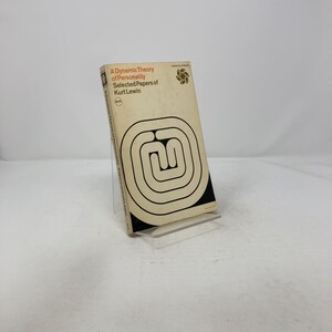 May include: A vintage paperback book titled "A Dynamic Theory of Personality Selected Papers of Kurt Lewin." The cover is beige with a black and white geometric design and the title in orange and black. A floral design is in the upper right corner.