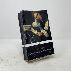 May include: A paperback copy of An Essay Concerning Human Understanding by John Locke, published by Penguin Classics. The black cover features a portrait of a person writing at a desk, with white text displaying the title and author name clearly.
