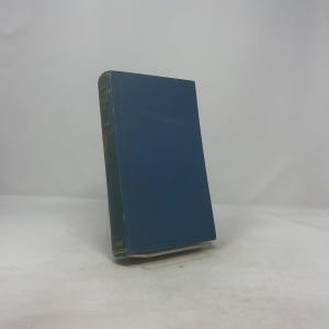 Puede incluir: Un libro de tapa dura azul con letras doradas en el lomo. El libro está apoyado en un soporte transparente. El título es parcialmente visible. La portada es de color azul liso.