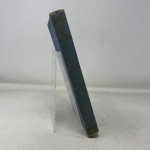Könnte beinhalten: Ein Vintage-Buch mit dem Titel "The Monarchs of War" von J.R. Green. Das Buch hat einen blauen Einband mit goldener Schrift und wird auf einem transparenten Acrylständer präsentiert. Der Buchrücken ist sichtbar und zeigt Titel und Autor.