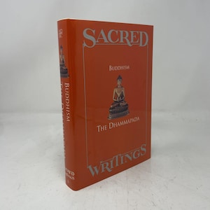 May include: A hardcover book titled Sacred Writings: Buddhism The Dhammapada with a bright orange cover. The front features silver text and a central illustration of a seated Buddha figure. The spine also displays the title in silver lettering.