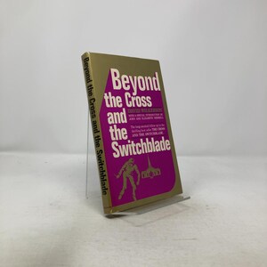 May include: A hardcover book titled "Beyond the Cross and the Switchblade" by David Wilkerson. The book has a gold cover with a magenta panel featuring the title and author's name. The spine also displays the title.