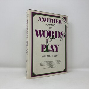 May include: A hardcover book titled "Another Almanac of Words at Play" by Willard R. Espy. The cover is cream-colored with a purple and green border. The title is in purple, with whimsical illustrations.