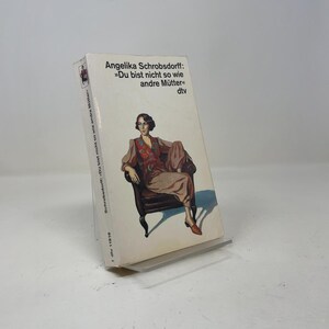 May include: A paperback book titled Angelika Schrobsdorff: Du bist nicht so wie andre Mütter published by dtv. The white cover features an illustration of a person with dark hair sitting in a dark armchair, wearing a patterned top and trousers.