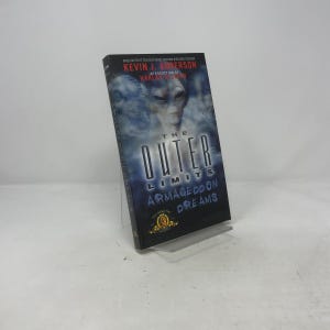Może przedstawiać: Twarda oprawa książki zatytułowana "The Outer Limits: Armageddon Dreams" autorstwa Kevina J. Andersona. Okładka przedstawia twarz kosmity i tekst "The Outer Limits" dużymi, pogrubionymi literami. Książka jest prezentowana na przezroczystym stojaku.