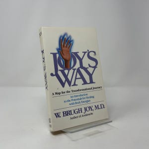 May include: A paperback book titled "Joy's Way" with a blue and brown graphic of a hand. The cover also includes the text "A Map for the Transformational Journey" and the author's name, W. Brugh Joy, M.D.