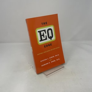 Può includere: Un libro arancione intitolato "The EQ Edge" con il testo "Emotional Intelligence and Your Success". La copertina presenta un design verde e bianco con le lettere "EQ". I nomi degli autori sono elencati di seguito.
