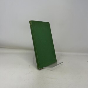 May include: A hardcover book with a solid green cover is displayed on a clear acrylic stand. The book's spine is visible, and the pages are not visible. The book is slightly angled, showcasing its cover and spine.