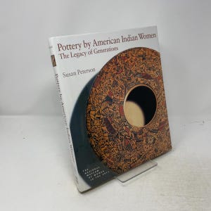 May include: A hardback book titled Pottery by American Indian Women: The Legacy of Generations by Susan Peterson. The white cover features a large, circular graphic of tan pottery with intricate black geometric patterns and a dark centre.