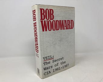 Puede incluir: Libro de tapa dura de Bob Woodward, titulado "VEIL: The Secret Wars of the CIA 1981-1987". El libro tiene una cubierta gris claro con letras rojas. El nombre del autor y el título son claramente visibles.