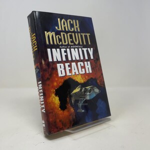 May include: A hardcover book titled Infinity Beach by Jack McDevitt. The cover features a dark blue and orange nebula-like background with a silver spaceship illustration. The author's name is in gold, and the title is in bold white lettering.
