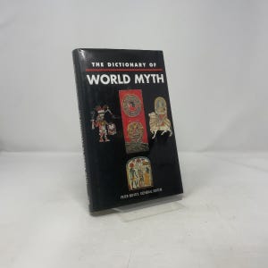 Puede incluir: Un libro de tapa dura titulado "The Dictionary of World Myth" con una cubierta negra. La cubierta presenta ilustraciones de varios artefactos culturales. El nombre del autor, Peter Bently, también es visible. El libro se muestra en un soporte transparente.