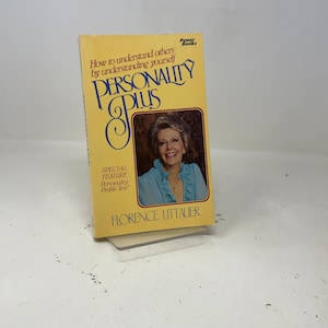 May include: A vintage paperback book titled "Personality Plus" by Florence Littauer. The cover is yellow with the title in large blue and gold lettering. A photo of a smiling woman is featured. The book is propped up on a clear stand.