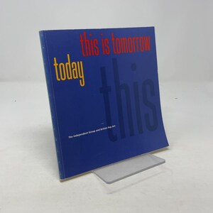 May include: A blue book titled "this is tomorrow" with the word "today" in yellow and "this" in red. The book is propped up on a clear plastic stand. The text "The Independent Group and British Pop Art" is printed at the bottom.