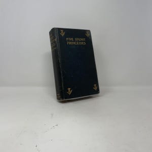 May include: A vintage book titled "Five Stuart Princesses" with a dark blue cover and gold lettering. The book has decorative gold thistle emblems on the cover. The book is slightly angled, showcasing its spine and cover details.