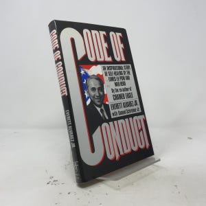 May include: A hardcover book titled Code of Conduct by Everett Alvarez Jr. with Samuel Schreiner Jr. The black cover features large white and red text, a portrait of a man, and a partial American flag graphic with descriptive text about the story.