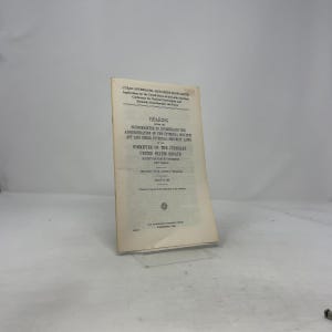 May include: A vintage document titled "Cuban Aftermath-Red Tide Blow South" with text including "Hearing" and "Committee on the Judiciary United States Senate." The document is aged with a light tan colour and is propped up on a clear stand.