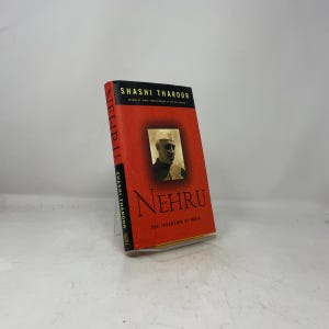 May include: A hardcover book titled Nehru: The Invention of India by Shashi Tharoor. The cover is bright red with a black top and side panel, featuring a black and white portrait of Jawaharlal Nehru in the center and gold text throughout.