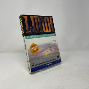 May include: A paperback book titled Linux Programming from the MIS:Press Slackware Series. The cover features large orange text, a sunset landscape, and a yellow starburst graphic stating Includes Slackware 96 Installation. Authors are listed.