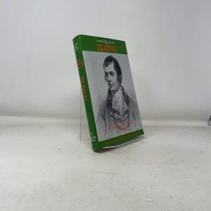 May include: A green covered book titled "Burns" from the Cambridge Edition series. The cover displays a portrait of a man and the title in orange. The book is propped up on a clear stand.