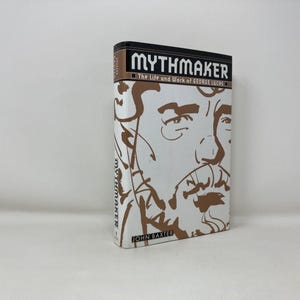 May include: A hardback book titled "MYTHMAKER" with a portrait on the cover. The spine is black with white text. The cover features a brown and white illustration of a man's face. The book is by John Baxter.
