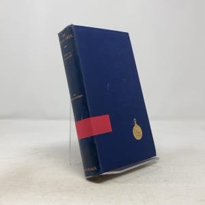 May include: A hardcover book titled "The Leaf Trek" by Eric A. Walker. The book has a dark blue cover with gold lettering and a gold emblem. A red band is wrapped around the spine. The book is displayed on a clear stand.