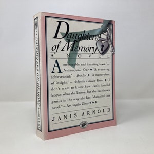 May include: A pink book cover with the title "Daughters of Memory" and the author's name "Janis Arnold". The cover features a keyhole with a key and a heart.