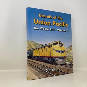 May include: Book titled "Diesels of the Union Pacific, The Classic Era - Volume 1" by Don Strack. The cover features a yellow and green diesel locomotive on a railway track, set against a blue sky and mountain backdrop.