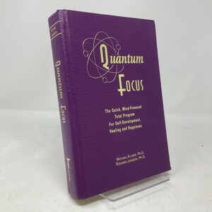 May include: A purple hardcover book titled "Quantum Focus" with a gold atom symbol on the cover. The book's subtitle is "The Quick, Mind-Powered Total Program for Self-Development, Healing and Happiness". The authors are Michael Ellner, Ph.D. and Richard Jamison, Ph.D.