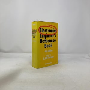 Puede incluir: Un libro amarillo titulado "Electronics Engineer's Reference Book, 4th Edition" de L.W. Turner. El título está en texto negro con un óvalo rojo alrededor. El libro está de pie.