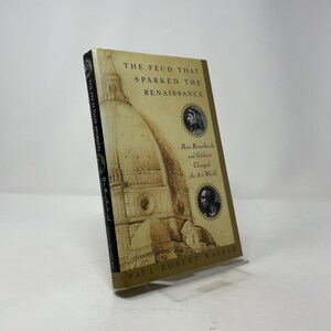 May include: A hardcover book titled "The Feud That Sparked the Renaissance" by Paul Robert Walker. The cover features a sepia-toned illustration of a cathedral dome and portraits. The book explores the impact of Brunelleschi and Ghiberti on art.
