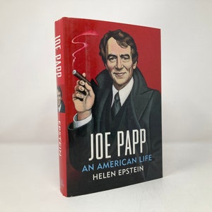 May include: A red hardcover book with a black and white illustration of Joe Papp on the cover. The title is "Joe Papp: An American Life" by Helen Epstein.