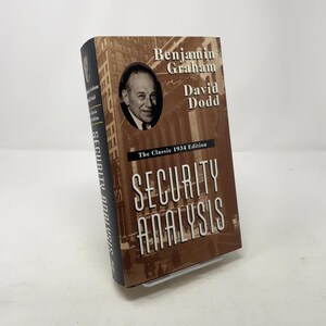 May include: A hardcover book titled "Security Analysis" by Benjamin Graham and David Dodd. The cover is brown with white text and a black spine. The book features a portrait of a man and the words "The Classic 1934 Edition".