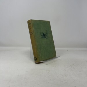 May include: A vintage book titled "The Countryman's Year" by David Grayson. The book has a green cover with gold lettering and a small illustration. The book is propped up on a clear stand.