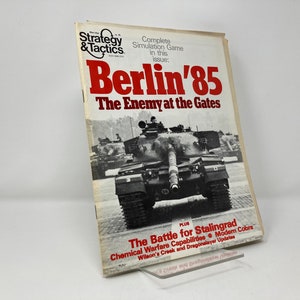 May include: A vintage issue of Strategy & Tactics magazine, titled "Berlin '85: The Enemy at the Gates." The cover features a tank and the magazine's logo. Additional text includes "The Battle for Stalingrad" and other military-related topics.