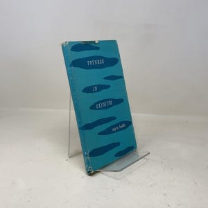 May include: A hardcover book titled "Toynbee in Elysium" by Myra Buttle. The book has a teal cover with the title in white and blue abstract shapes. The book is displayed on a clear acrylic stand.