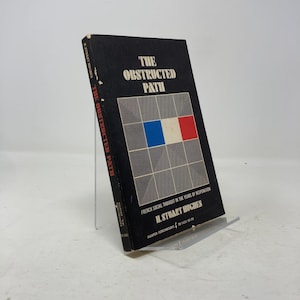 May include: A hardcover book titled "The Obstructed Path" by H. Stuart Hughes. The cover is black with white text and a geometric design incorporating blue, white, and red squares. The book is displayed on a clear stand.