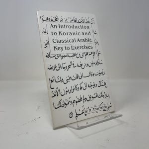 May include: A white softcover book titled An Introduction to Koranic and Classical Arabic Key to Exercises by W. M. Thackston. The cover features black Arabic calligraphy printed over the entire surface, with the English title in a central box.