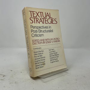 以下が含まれることがあります： Josué V. Harari編集の「Textual Strategies: Perspectives in Post-Structuralist Criticism」というタイトルのクリーム色のソフトカバー本。表紙には濃い赤と黒の文字で、ロラン・バルトやミシェル・フーコーなどの寄稿者名が記載されています。