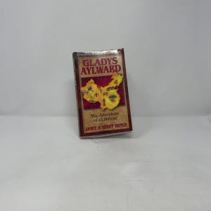 May include: A hardcover book titled "Gladys Aylward" with a map of China on the cover. The book's cover is a mix of red, brown, and gold tones. The text "The Adventure of a Lifetime" and the author's names are also visible.