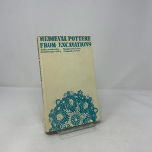 May include: A vintage book titled "Medieval Pottery From Excavations" with teal text and a teal decorative design. The book has a cream-colored cover and is propped up on a clear stand.