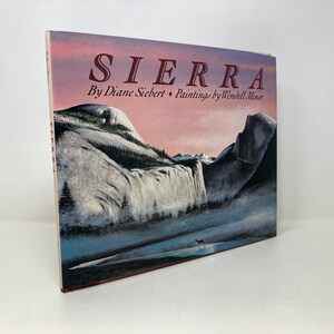 Puede incluir: Un libro titulado "SIERRA" de Diane Siebert con pinturas de Wendell Minor. La portada presenta un paisaje escénico con una cascada, montañas y un ciervo en primer plano.